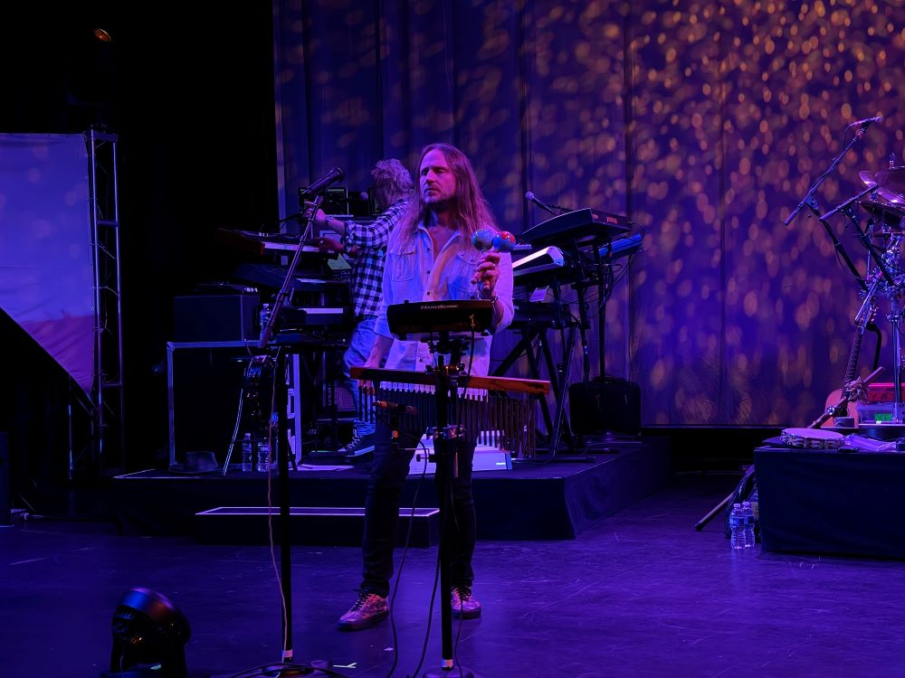 A person on stage with microphone and musical instruments Description automatically generated