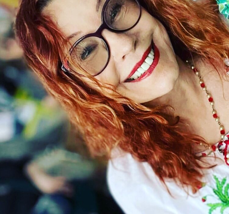 A person with red hair and glasses smiling Description automatically generated