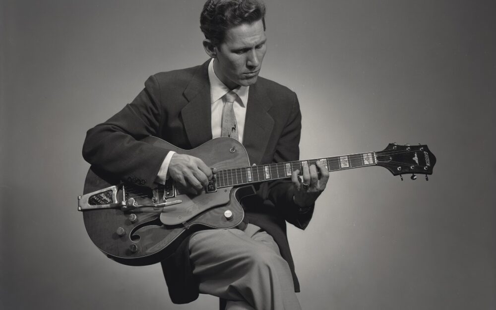 A person in a suit playing a guitar Description automatically generated