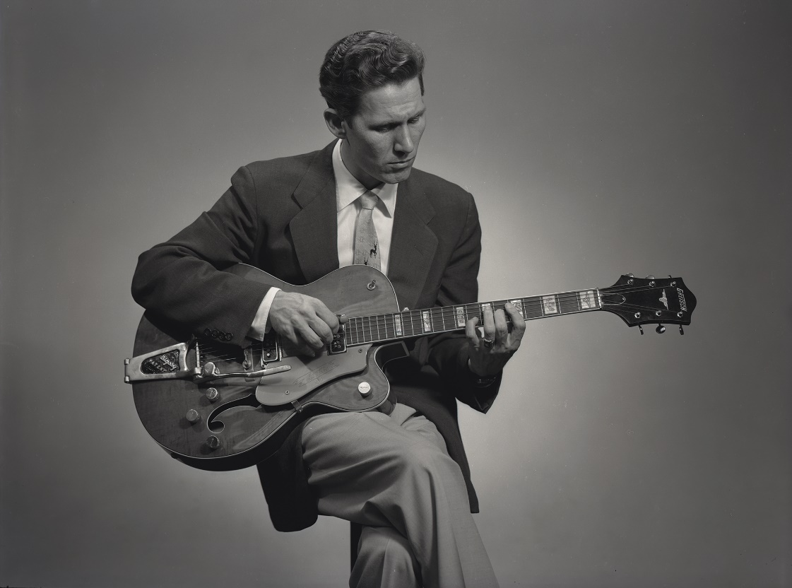 A person in a suit playing a guitar

Description automatically generated