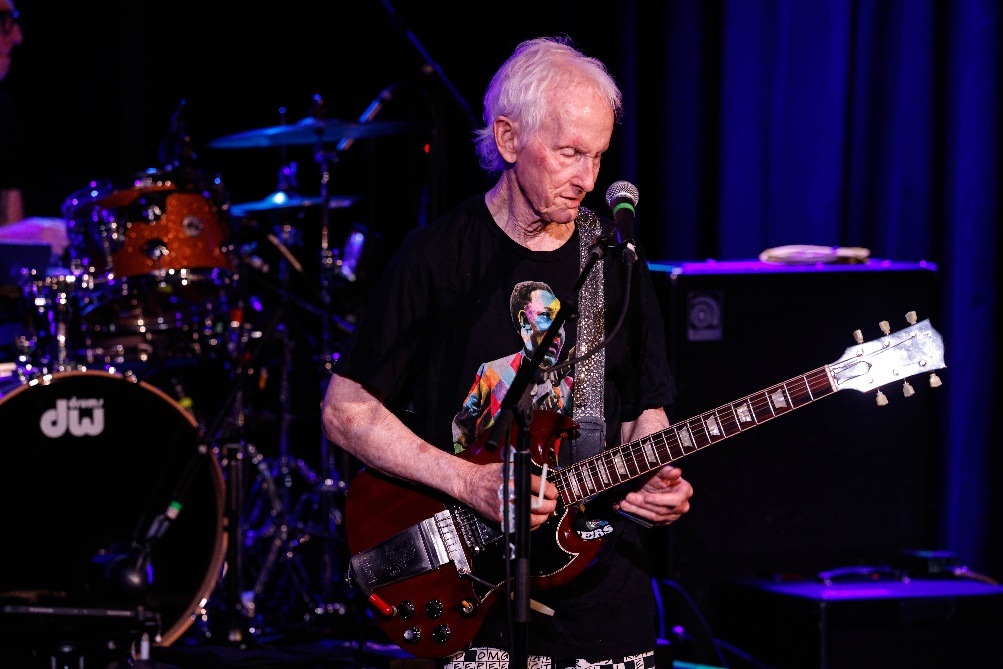 An old person playing guitar on stage

AI-generated content may be incorrect.