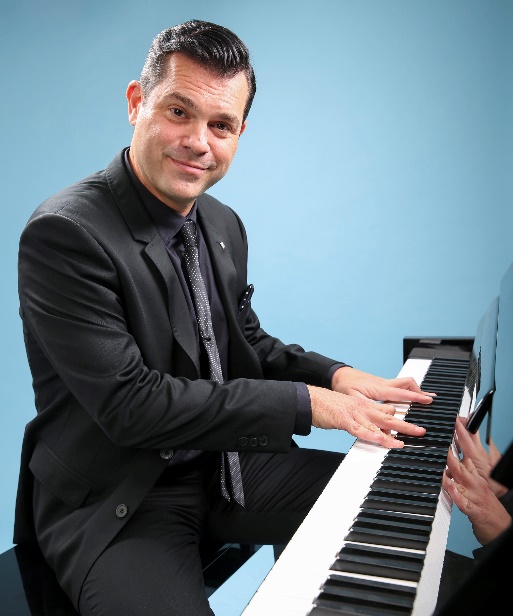 A person in a suit playing a piano
Description automatically generated