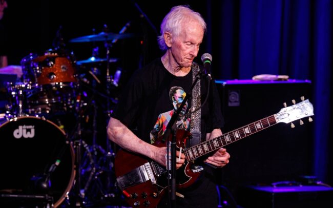 An old person playing guitar on stage AI-generated content may be incorrect.